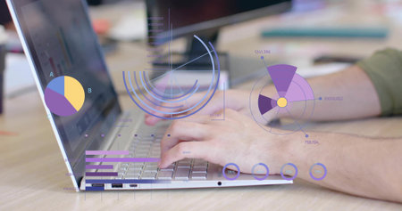 Typing man wearing olive shirt tapping keys on silver laptop at office desk showing data charts....