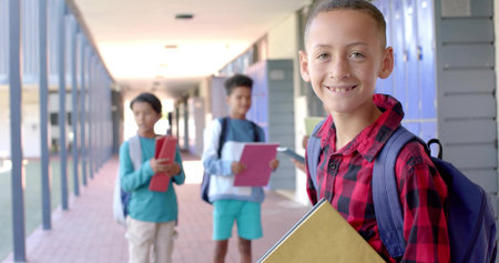 Smiling boy in red plaid shirt holding yellow folder walking school hall, with lockers, copy space....