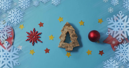 Arranging cork-tree ornament sitting on blue surface, with red bauble, snowflake cutouts, ribbon....