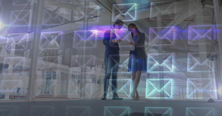 Examining tablet, two colleagues in suits and heels in warehouse office, with envelope overlays....