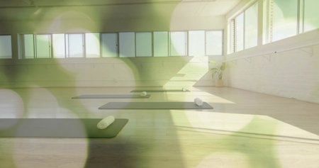 Displaying empty yoga studio featuring dark mats on wood floor, featuring windows and rolled towels....