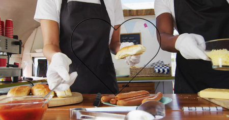 Preparing two servers assembling buns and dogs at counter, in white shirts and aprons, heart frame....