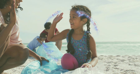 Smiling braided girl raising hand on beach, wearing blue top, pink leggings, blue fabric, bubbles....