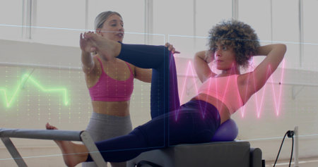 Performing woman crunching on reformer on ball at studio, instructor holding leg, in pink tops....