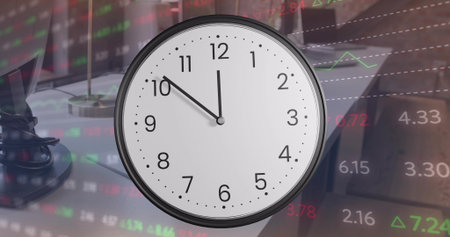 Showing large round analog clock dominating office desk with lamp, cable, laptop, market tickers....