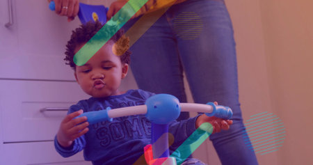 Puckering blue-shirted baby gripping bar on ride-on at home by drawers, with denim and overlays....