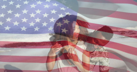 Smiling couple standing at beach shore in light top and patterned shirt with translucent flag....