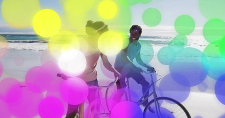 Cycling couple riding along sandy shoreline in sunny day, tanks, shorts, cruiser bikes, color discs....