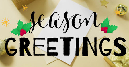 Showing white card and envelope with black season GREETINGS text on beige tabletop, gold bauble....