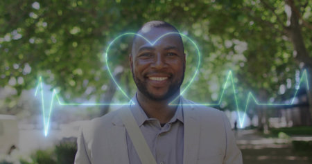 Smiling man wearing beige jacket and bag strap, standing on sunlit park walkway with neon EKG. Headshot, professional, outdoor, urban, mature, suit, heartbeatの写真素材