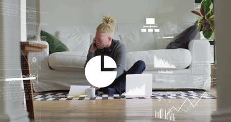 Holding smartphone, man wearing gray knit reviewing papers on living room rug with laptop overlays....