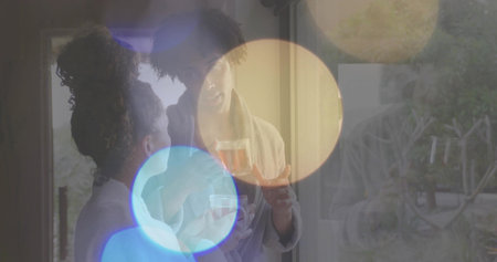 Standing near glass door, couple in light robes holding glass mug and cup, speaking amid bokeh....