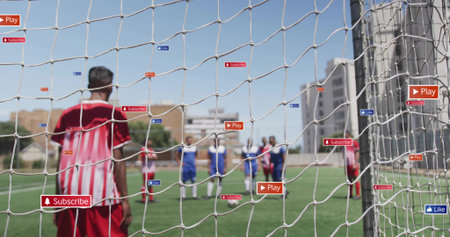 Standing player in red-white jersey watching play near goal net at urban pitch, Play Subscribe Like....