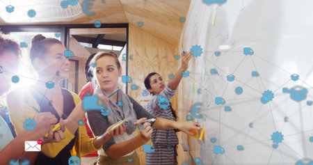 Designing team wearing casual attire placing sticky notes on whiteboard in studio with blue overlay....