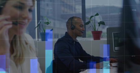 Typing man in navy shirt and headset at office desk, viewing monitor with bar-chart overlay....