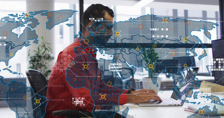 Analyzing network data, Middle Eastern man in red shirt working at desk with laptop, monitors, map....