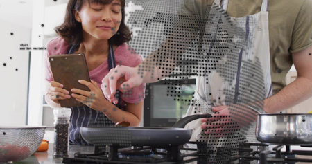 Cooking couple wearing aprons stirring frying pan on gas cooktop at home kitchen, holding tablet. Halftone, modern, cozy, duo, device, culinary, lifestyleの写真素材