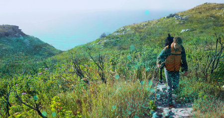 Hiking man wearing green jacket with backpack and trekking pole on narrow coastal trail, copy space. Hiker, sea, path, hills, wildflowers, shrubs, packの写真素材