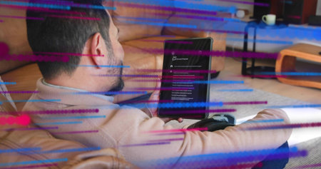 Holding tablet, Asian man wearing beige sweater sitting on tan sofa scrolling screen, color streaks....
