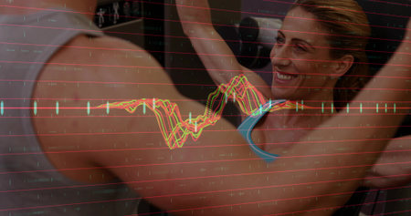 Vertical video: Smiling woman in blue sports top raising arms in gym after partner cue, with chart....