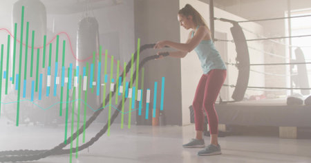 Working woman wearing light blue tank top maroon leggings whipping battle ropes in gym, copy space....