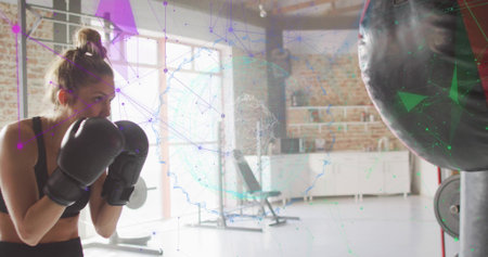 Facing punching bag, woman in black sportswear holding black boxing gloves in gym, mesh, copy space. Fitness, training, athlete, studio, urban, industrial, contemporaryの写真素材