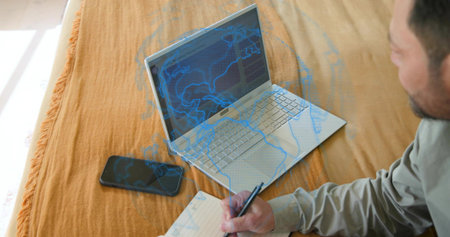 Writing mature man wearing gray shirt, leaning on bed, using silver laptop and notebook, copy space....