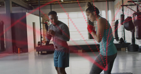 Training coach guiding trainee throwing punches in warehouse gym, wearing teal top and red wraps....