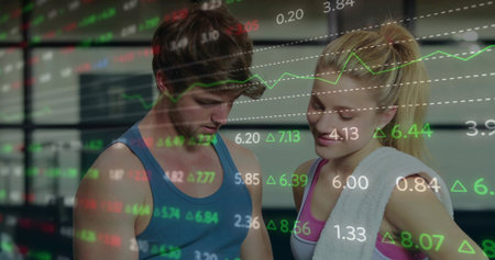 Standing man left and woman right gazing down in gym in sportswear, white towel, financial charts. Fitness, workout, partnership, analytics, data, overlay, focusの写真素材