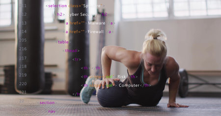 Balancing mid-adult woman in dark workout outfit on medicine ball on gym mat, punching bag visible....