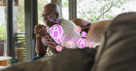 Sitting senior man wearing glasses, gray shirt on sofa at home, viewing pink purple hologram nodes. Augmented, network, thoughtful, lounge, sunlit, greenery, conversationの写真素材