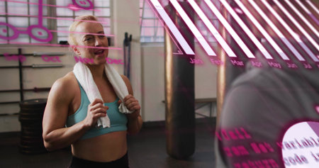 Workout partners pausing in gym near pink overlay partition, woman in blue sports bra holding towel....