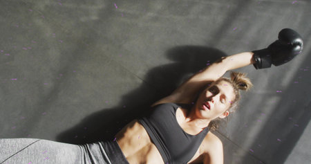 Lying boxer catching breath on gym floor with shadows showing abs wearing sports bra leggings glove....