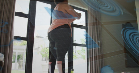 Facing woman wearing peach tank and black leggings at glass doors with green bottle, blue overlays. Fitness, workout, minimalist, daylight, home, patio, gridの写真素材