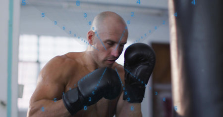 Training shirtless boxer boxing heavy bag in gym under window with blue grid wearing black gloves....