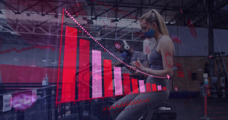 Pedaling woman in athletic wear masked at warehouse gym, with stationary bike and red chart overlay....