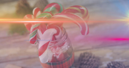 Glass jar wearing lace and plaid ribbon, holding candy canes with pine cones, lens flares. Stilllife, rustic, festive, warm, cozy, tabletop, bokehの写真素材