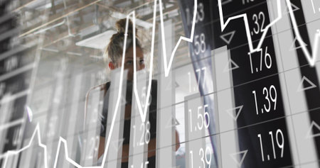 Studying female analyst behind glass partition in dark blazer, reading overlaid charts with numbers....