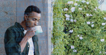 Green-shirted man sipping mug on terrace beside wall and vine, with blue binary overlay, copy space....