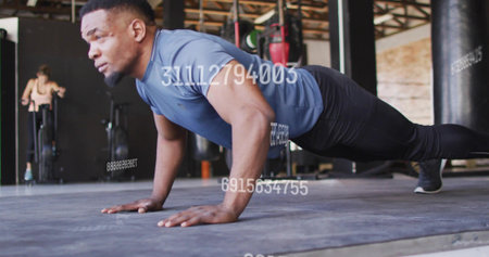Holding muscular man holding plank on padded mat at gym, wearing blue top, numeric overlay. Studio,...