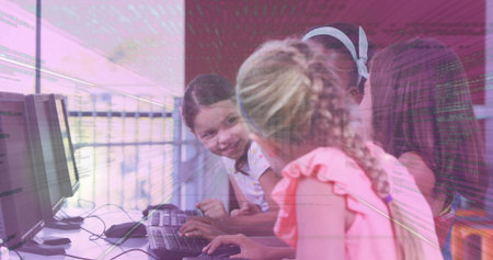 Typing girls gathering at row of computers in lab, one wearing pink ruffled top, holding infant....