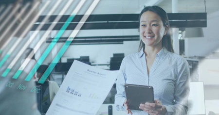 Smiling Asian woman wearing blue blouse holding tablet, presenting quarterly report in office....