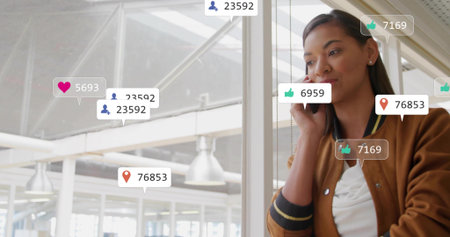 Holding smartphone, brown-jacket woman badged leaning by glass in office with metrics, copy space....