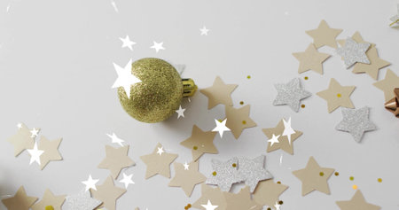Resting gold glitter bauble on white flatlay, surrounding beige and silver star confetti, metal bow....
