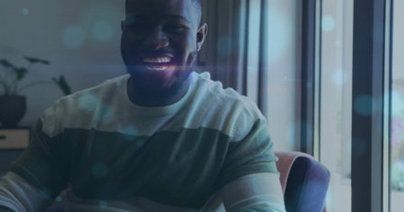 Smiling adult man wearing striped crewneck sweater sitting in armchair by tall window, lens flare....