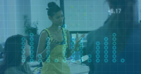 Gesturing female presenter speaking at conference room in yellow sleeveless dress with data overlay....