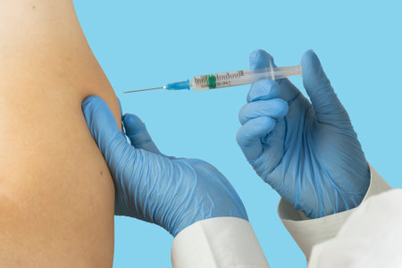 The doctor gives an injection to the patient. Doctors hands in blue gloves with an injection in one...