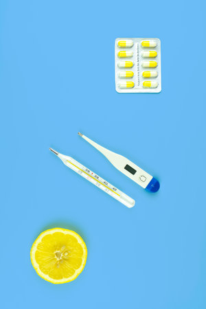 Two thermometers, pills and a slice of lemon on a blue background. Everyday objects of a sick...