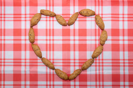 The cookies are arranged in the shape of a heart on a table covered with a white and red checkered tablecloth. Baking top view. The concept of Valentines Day.の写真素材