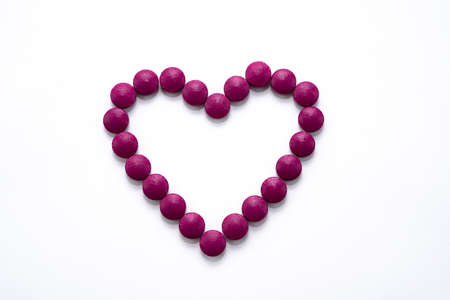 Heart laid out of burgundy tablets for Valentines Day. Medical drugs on a white background. Protect...